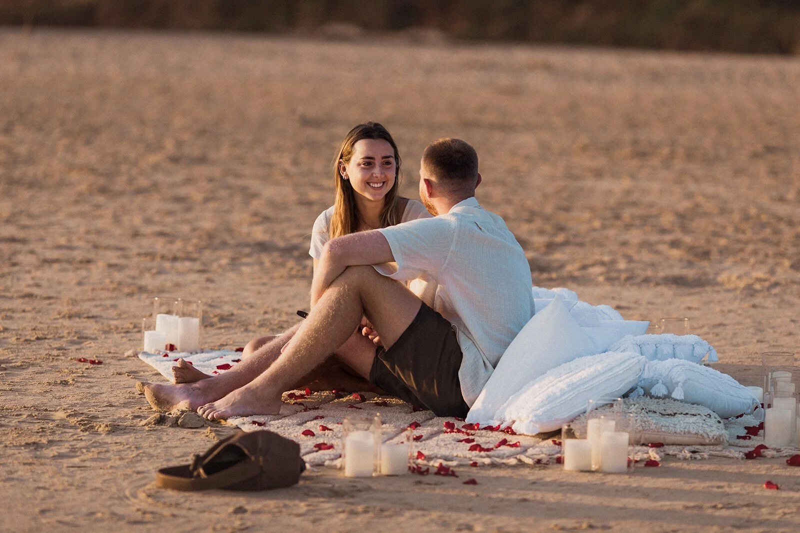 Couple sitting and chatting on the blanket among pillows and candles, Charlie and Hannah's sunrise marriage proposal at Broken Head Beach, Byron Bay