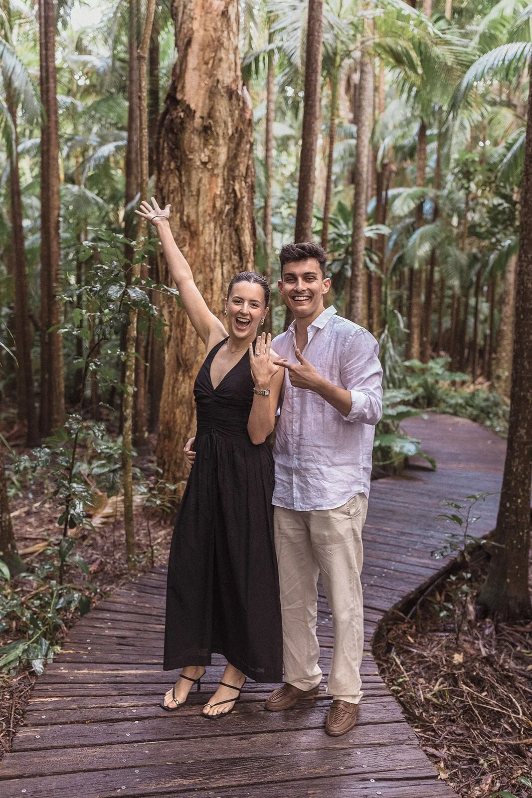 Woman raising her hand in delight to show her engagement ring on the boardwalk, Ben and Chloe's marriage proposal in Byron Bay