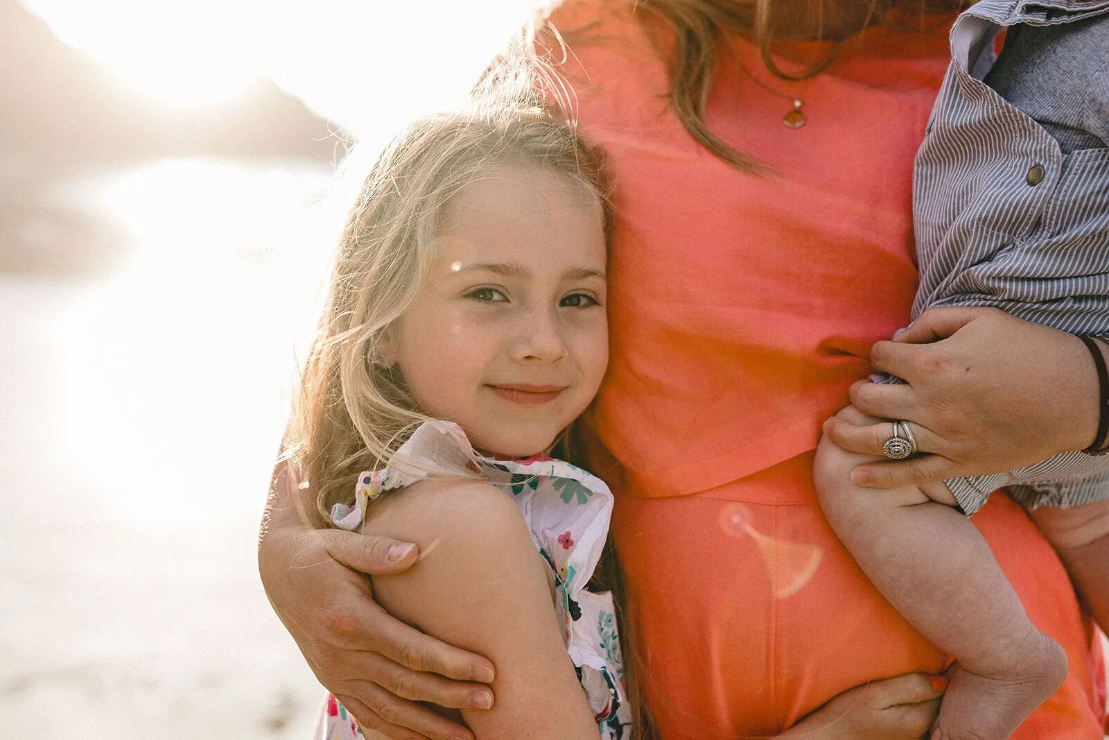 Girl with blonde hair held close in a family hug, glowing in backlit golden light