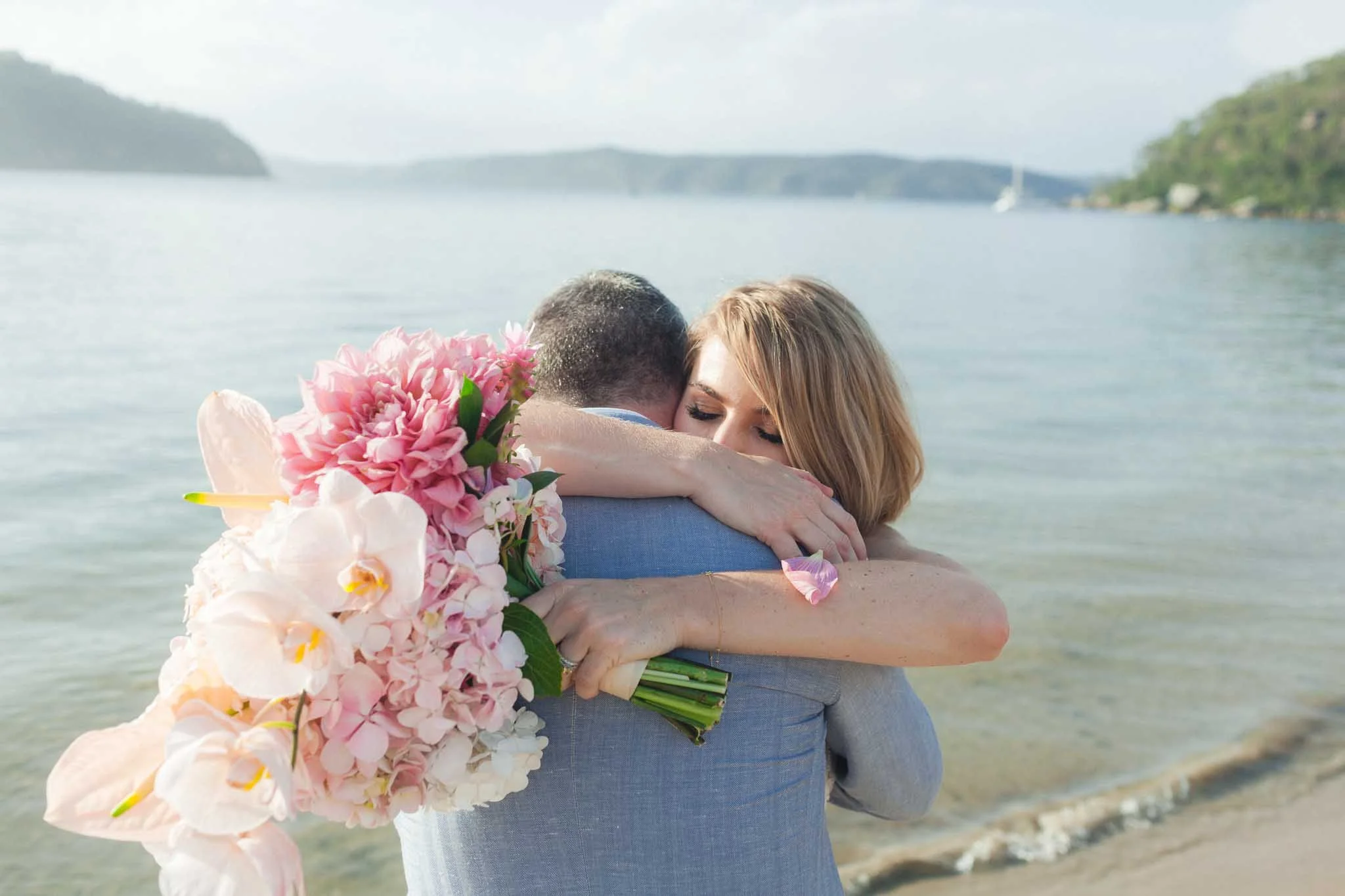 A bride’s embrace by the water at Palm Beach, pink bouquet in hand