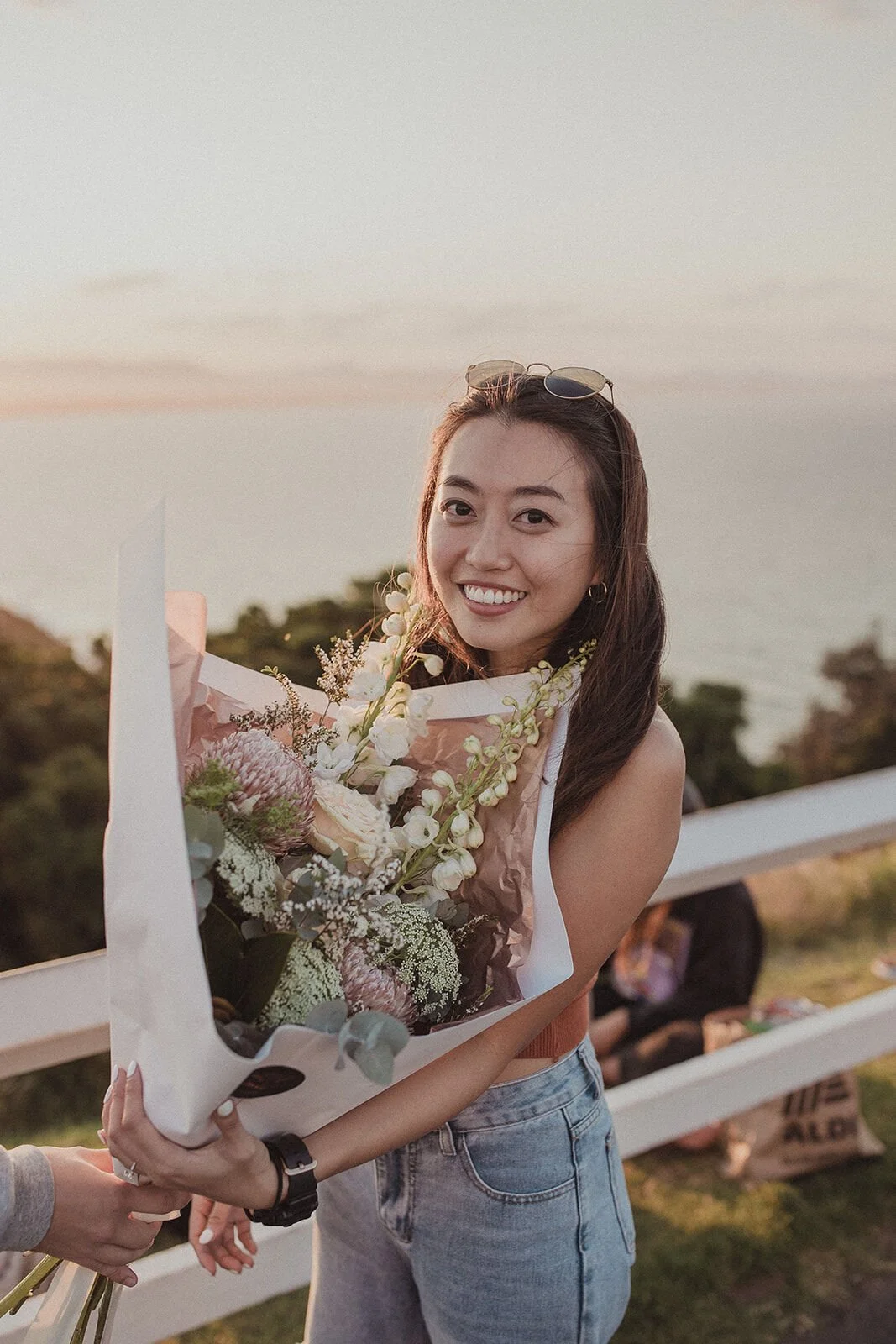 Woman smiling at the camera with a bouquet in the sunset light, Douglas and Ying's sunset marriage proposal at Cape Byron Lighthouse, Byron Bay