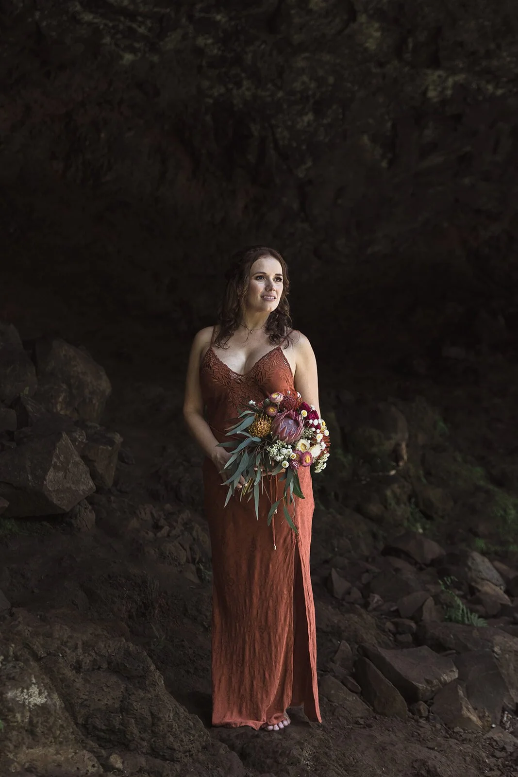 Bride in a rust dress with her bouquet in the cave, Sara and Graeme's elopement at Killen Falls, Northern Rivers