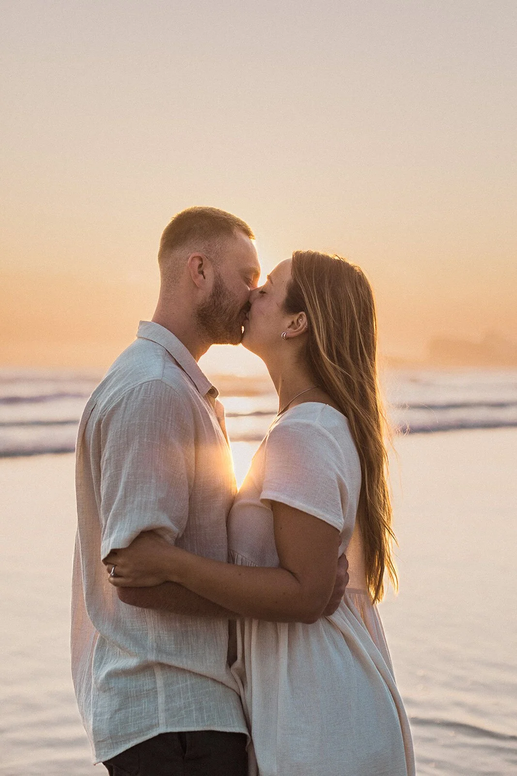 Couple kissing with the sunrise glowing between them, Charlie and Hannah's sunrise marriage proposal at Broken Head Beach, Byron Bay