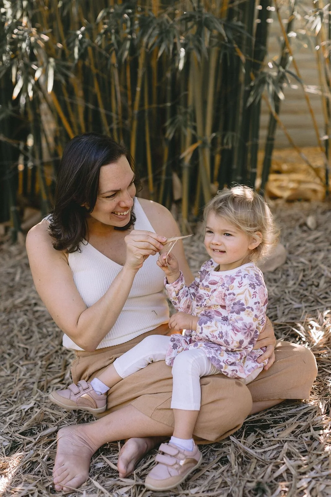 Mum sitting cross-legged with her toddler daughter on her lap, laughing together