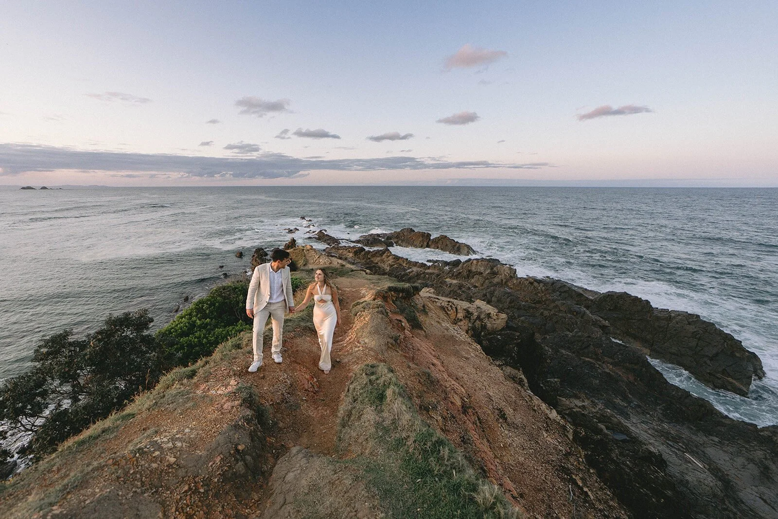 Couple holding hands on the headland ridge, Abby and James' elopement at Little Wategos Beach, Byron Bay