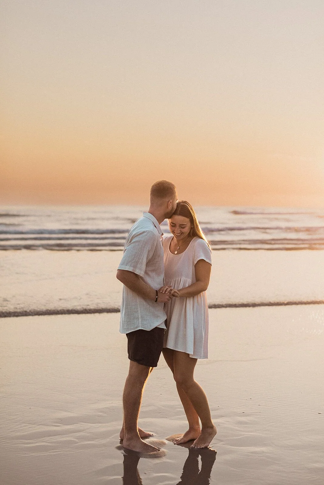 Couple holding hands and smiling in the golden sunrise light, Charlie and Hannah's sunrise marriage proposal at Broken Head Beach, Byron Bay