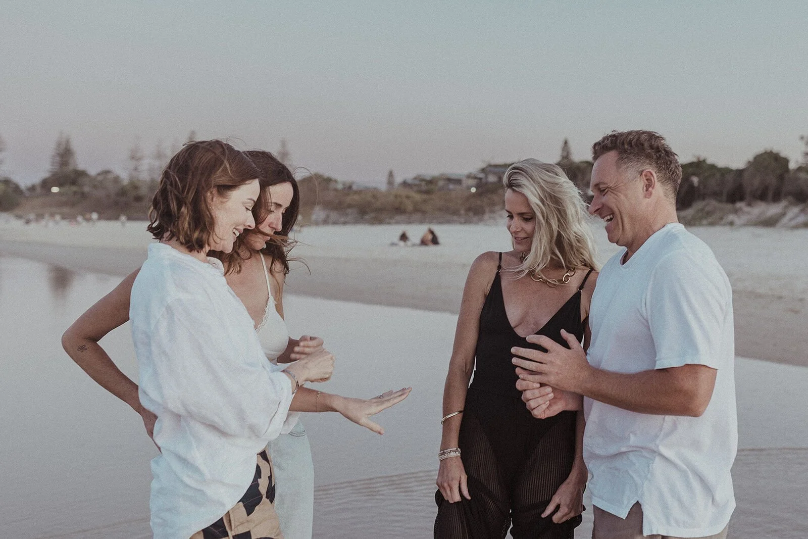 Couple laughing with friends on the shoreline, Jamie and Jessica's beach marriage proposal at Belongil Beach, Byron Bay