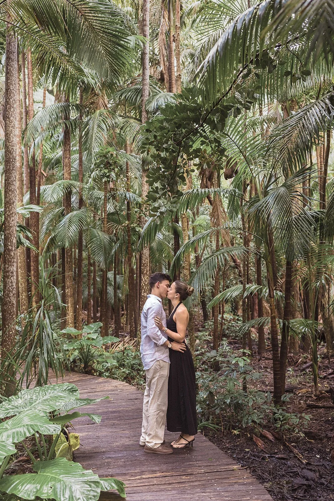 Couple kissing on a timber boardwalk through the rainforest, Ben and Chloe's marriage proposal in Byron Bay