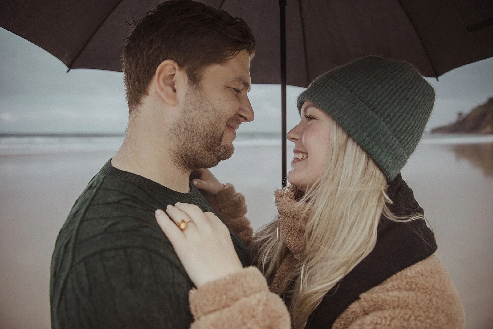 Couple smiling nose to nose with her ringed hand on his chest, Raphael and Vany's rainy day marriage proposal at Broken Head Beach, Byron Bay