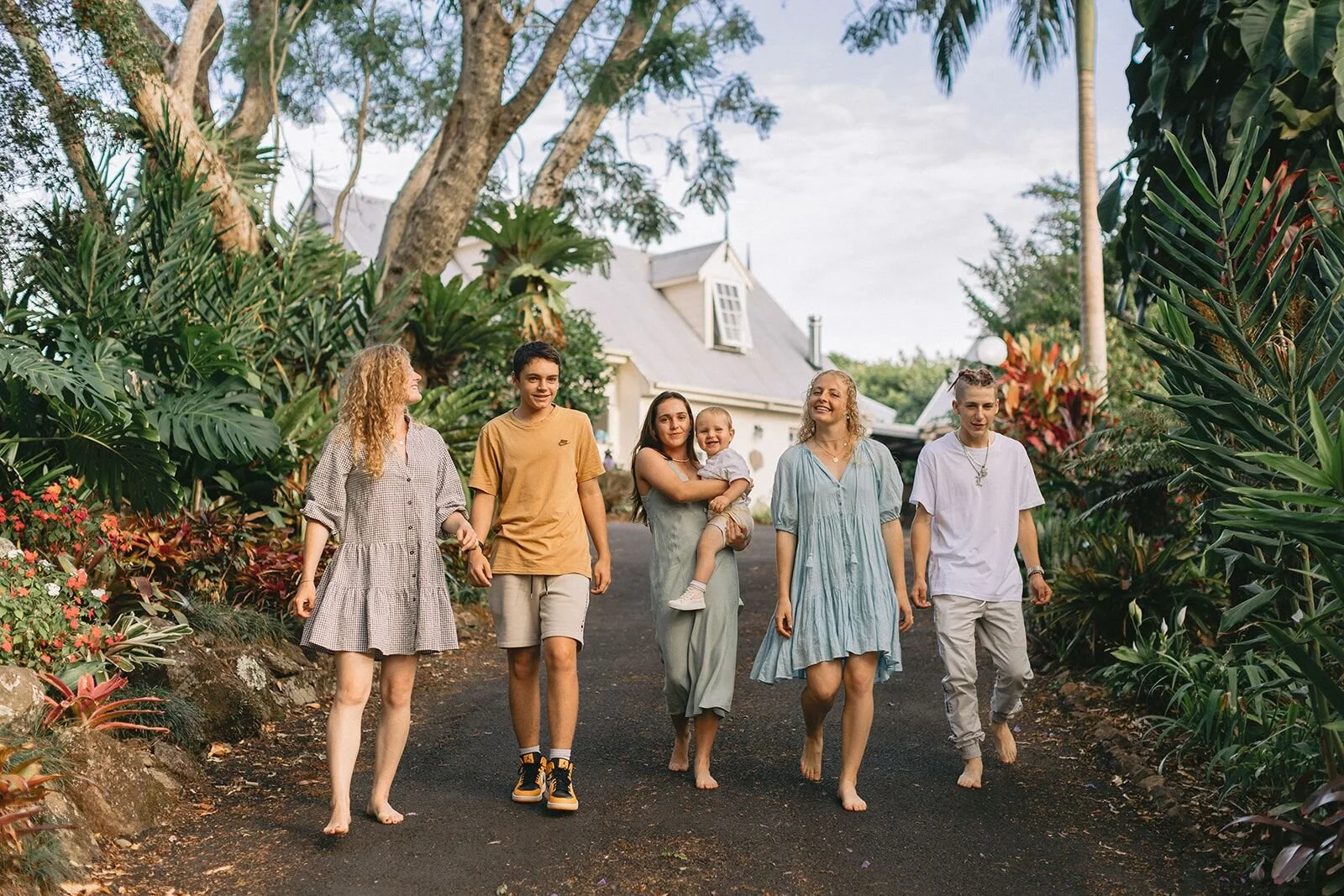Family walking together down a driveway lined with tropical garden toward the homestead