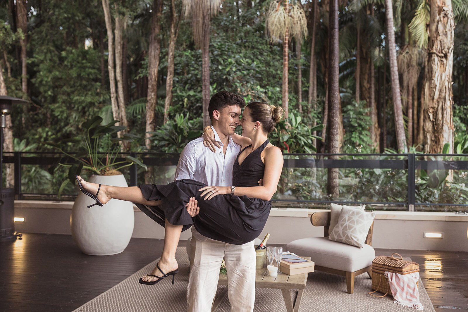 Man carrying his fiancée with foreheads touching on the deck, Ben and Chloe's marriage proposal in Byron Bay