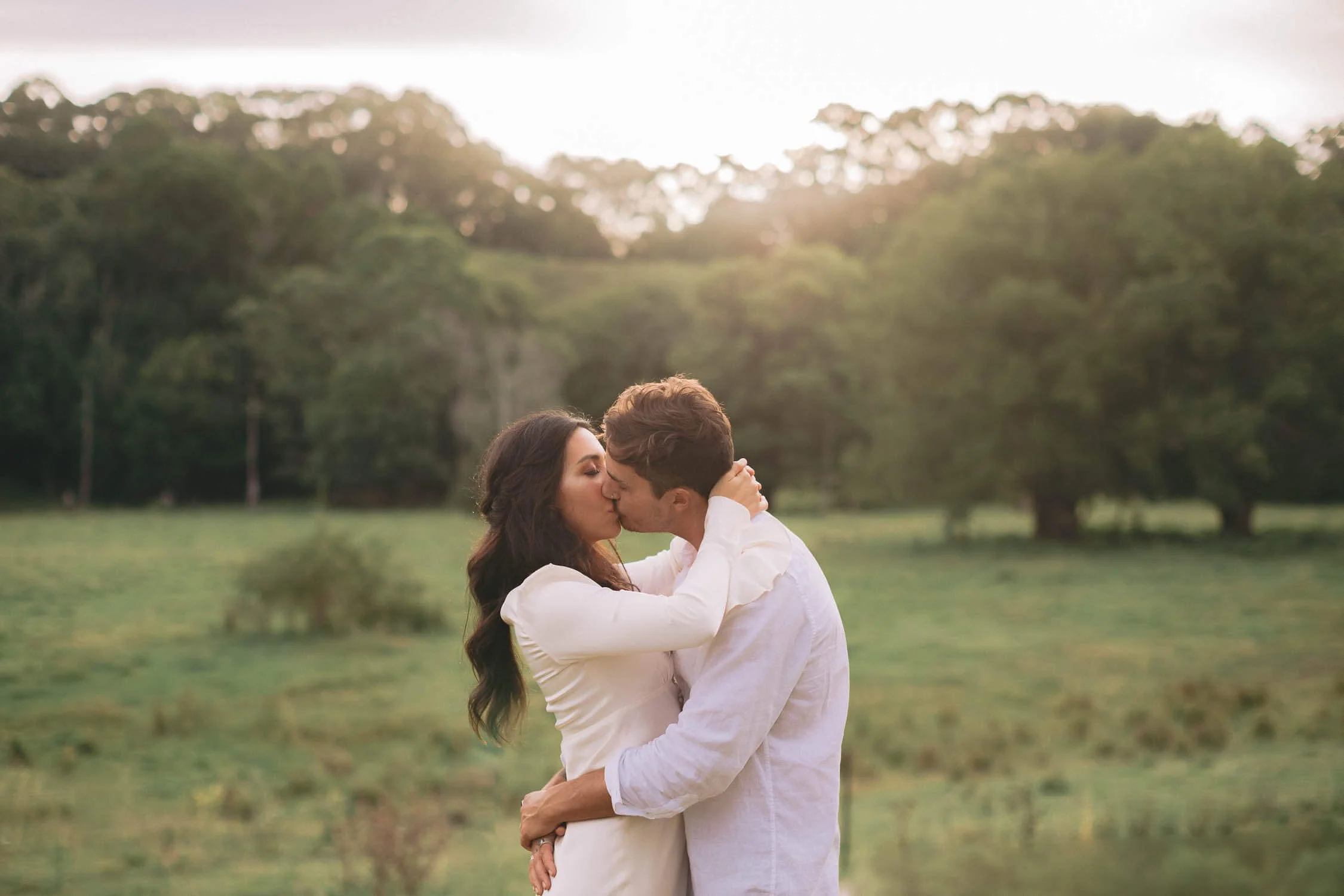 Couple kissing in a hinterland paddock at golden hour on their Byron Bay elopement