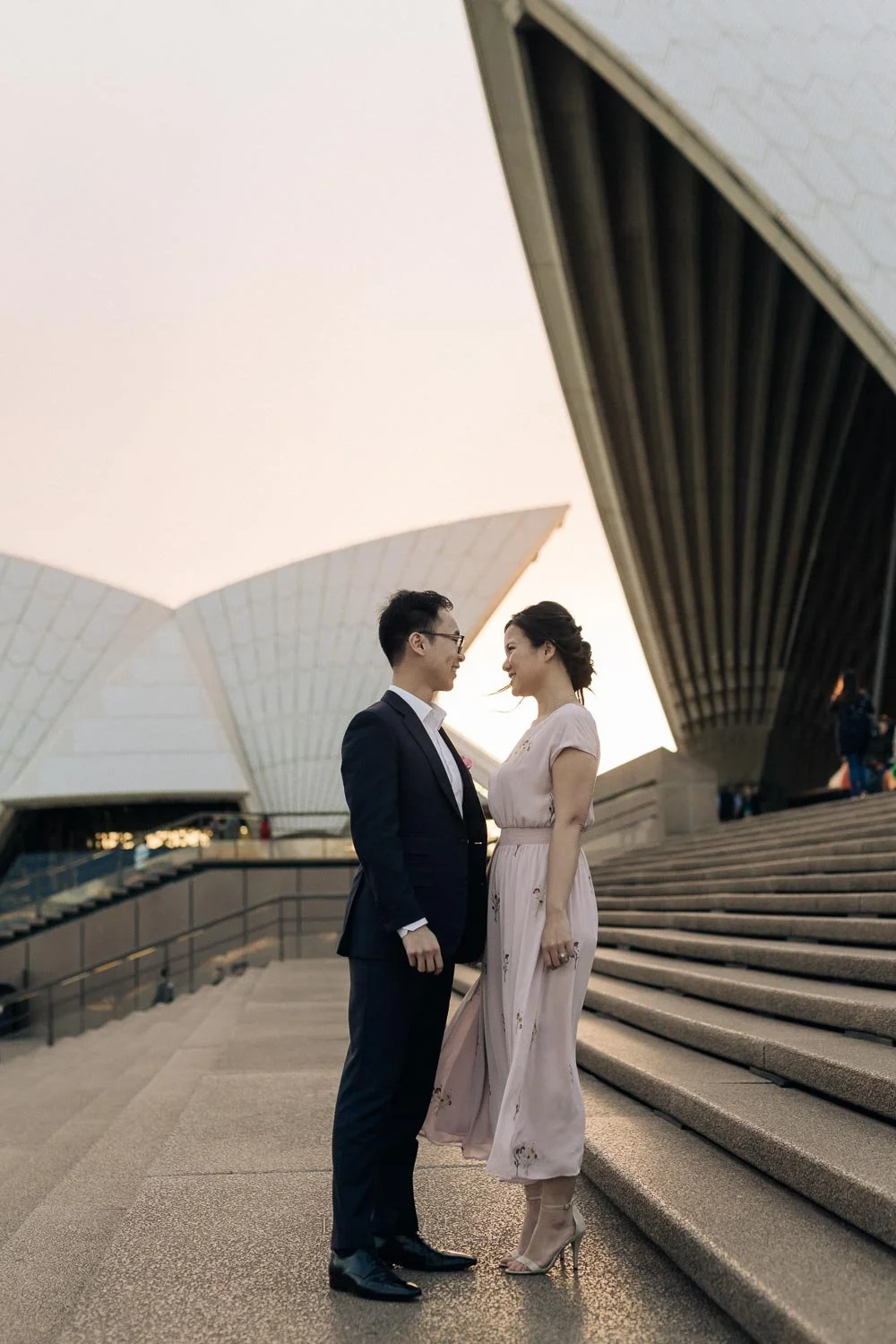 Couple standing beneath the Sydney Opera House sails on the forecourt steps