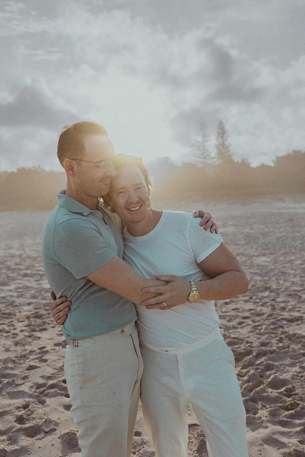 Couple hugging and laughing in golden light on the sand, Byron and Luke's marriage proposal at Cabarita Beach, Northern Rivers