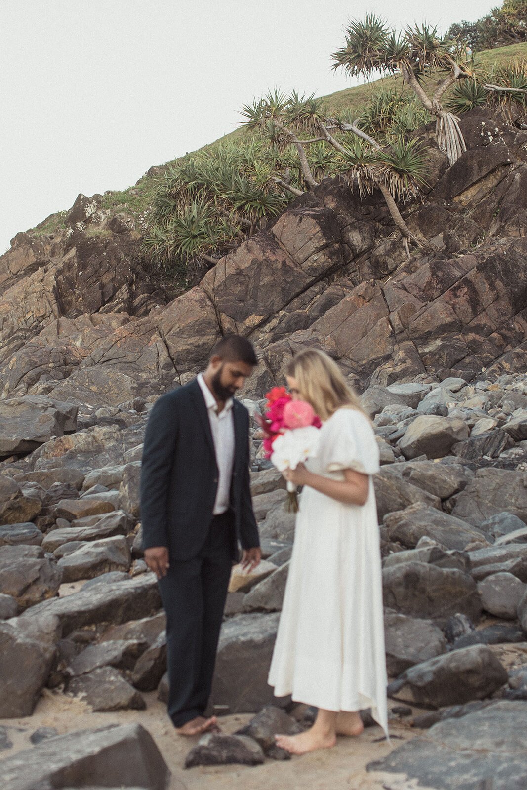 Couple standing among the rocks and smelling the bouquet, Brittany and Mark's elopement at Cabarita Beach, Northern Rivers