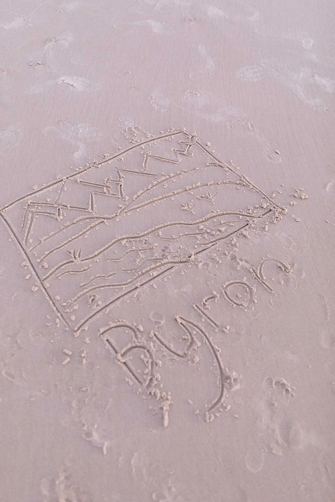 A flag and the word Byron drawn in the sand, a keepsake from the family shoot at Wategos