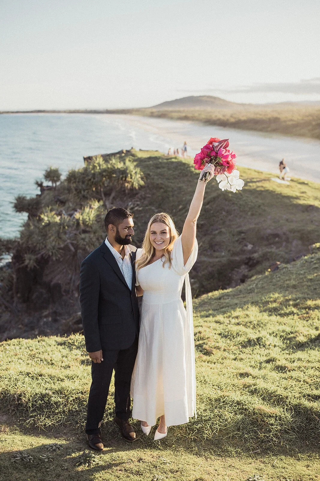Bride raising her bouquet in celebration beside the groom, Brittany and Mark's elopement at Cabarita Beach, Northern Rivers