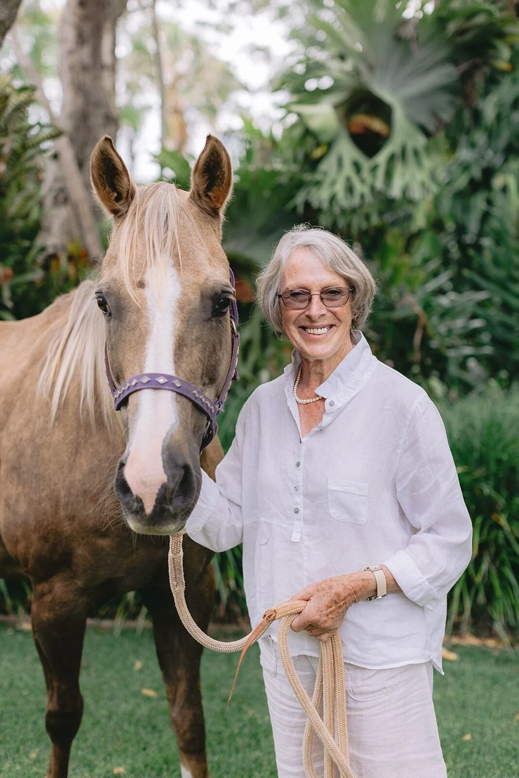 Grandmother in white linen smiling beside her palomino horse at Possum Creek, Byron Bay hinterland
