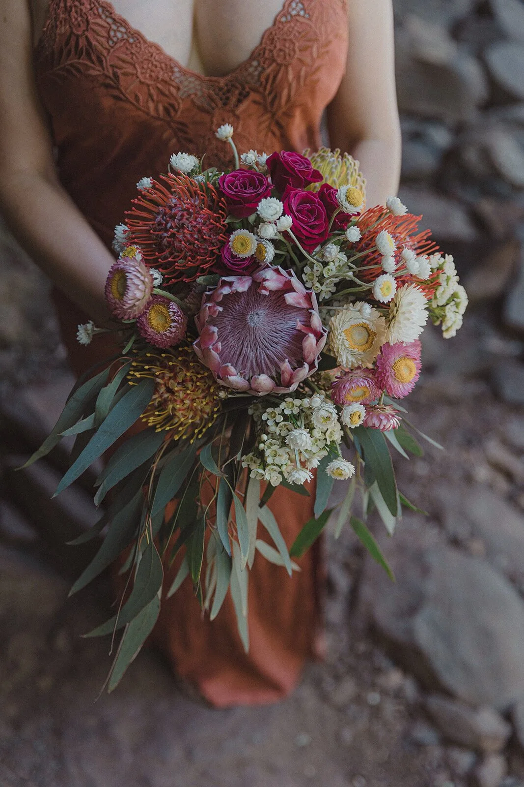 Detail of the bouquet held against a rust dress, Sara and Graeme's elopement at Killen Falls, Northern Rivers