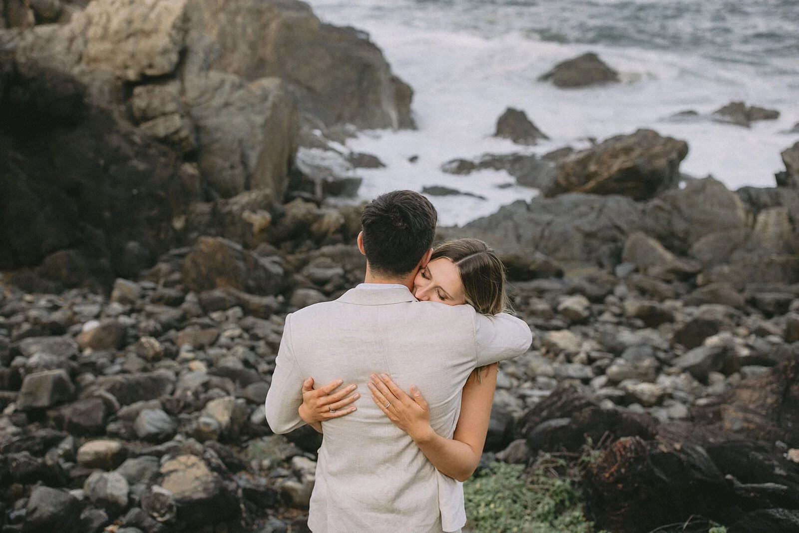 Bride hugging the groom on a rocky shoreline, Abby and James' elopement at Little Wategos Beach, Byron Bay