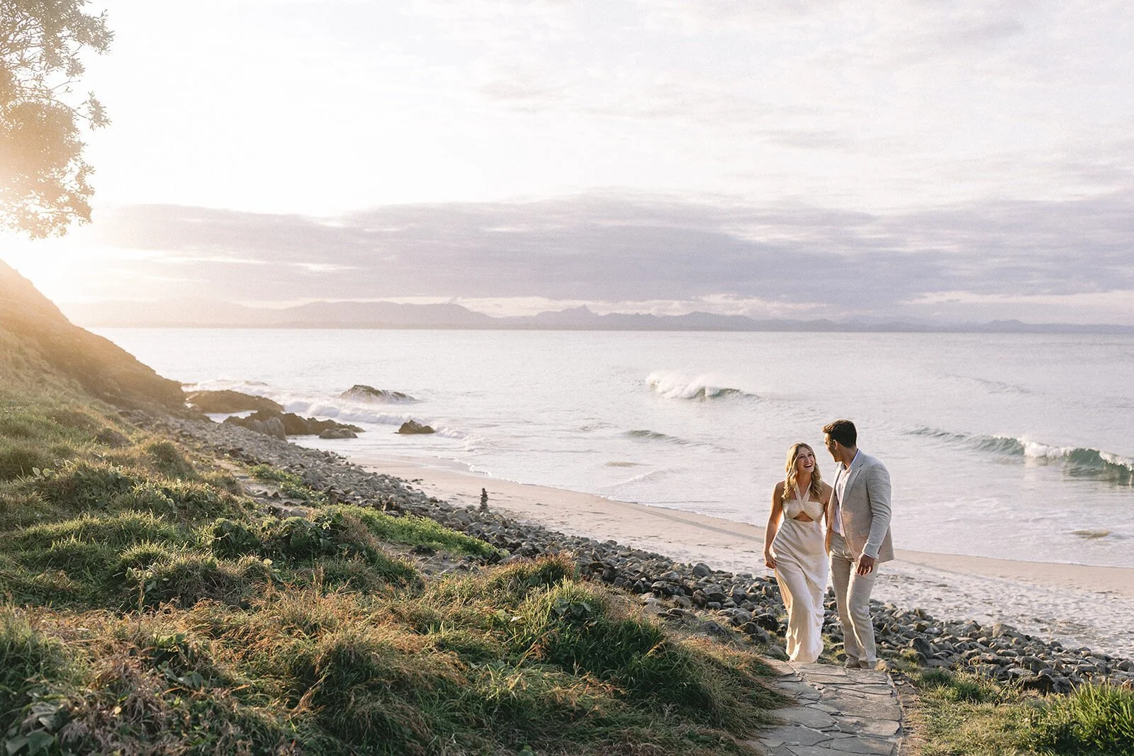 Couple walking up the coastal path above the beach at sunset, Abby and James' elopement at Little Wategos Beach, Byron Bay