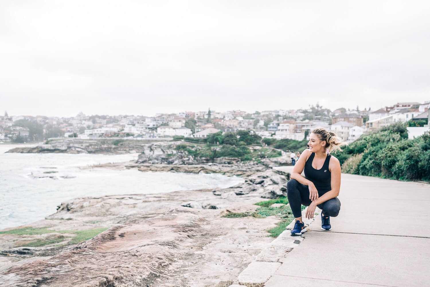Woman crouching on the coastal rocks above Bondi Beach