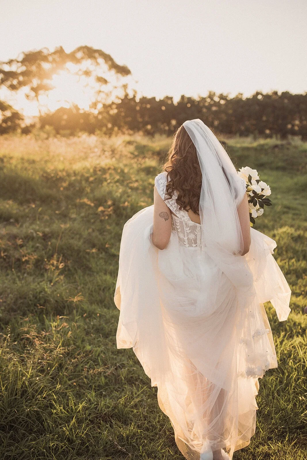 Bride in a veil walking through the sunset paddock, Steph and William's wedding at Earth House, Byron Bay