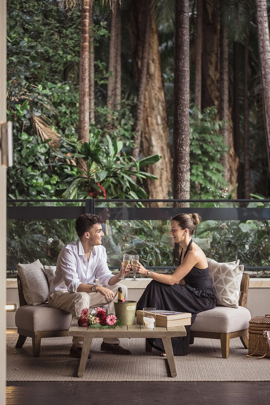 Couple toasting on the lounge with flowers on the table, Ben and Chloe's marriage proposal in Byron Bay