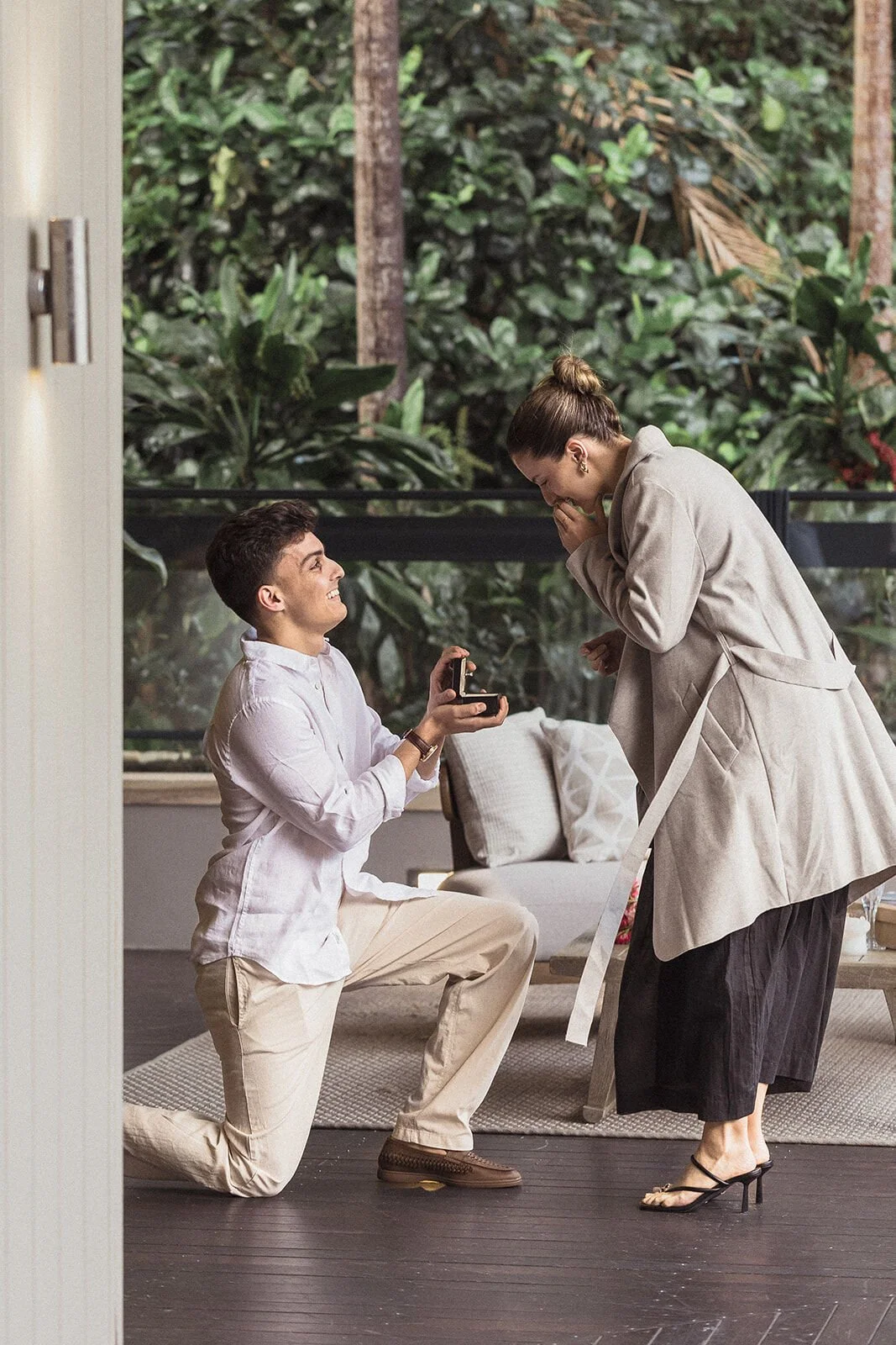 Man on one knee holding the ring box as the woman covers her mouth in surprise, Ben and Chloe's marriage proposal in Byron Bay