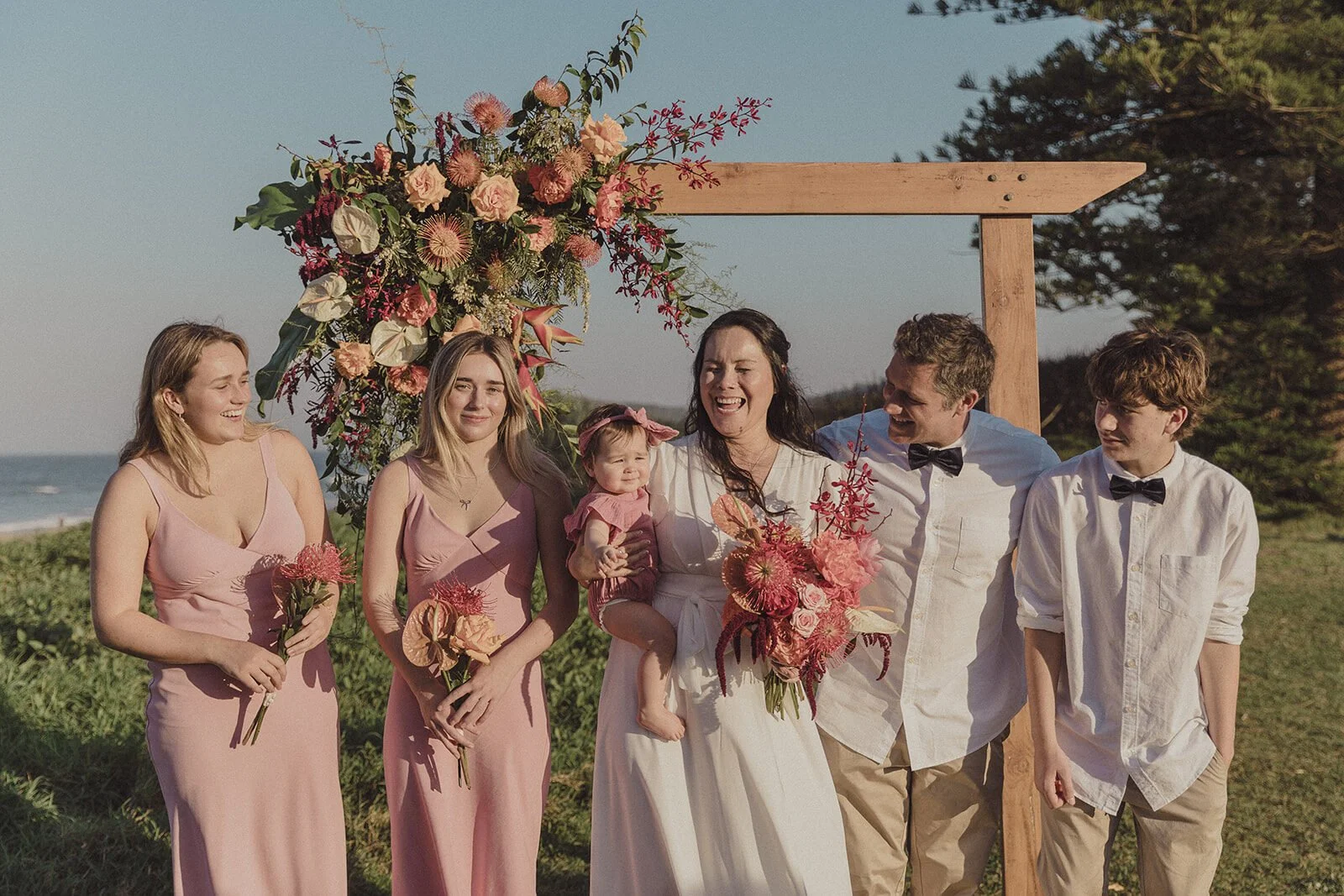 Family laughing together beside the arch, Maritess and Mark's elopement at Lennox Head
