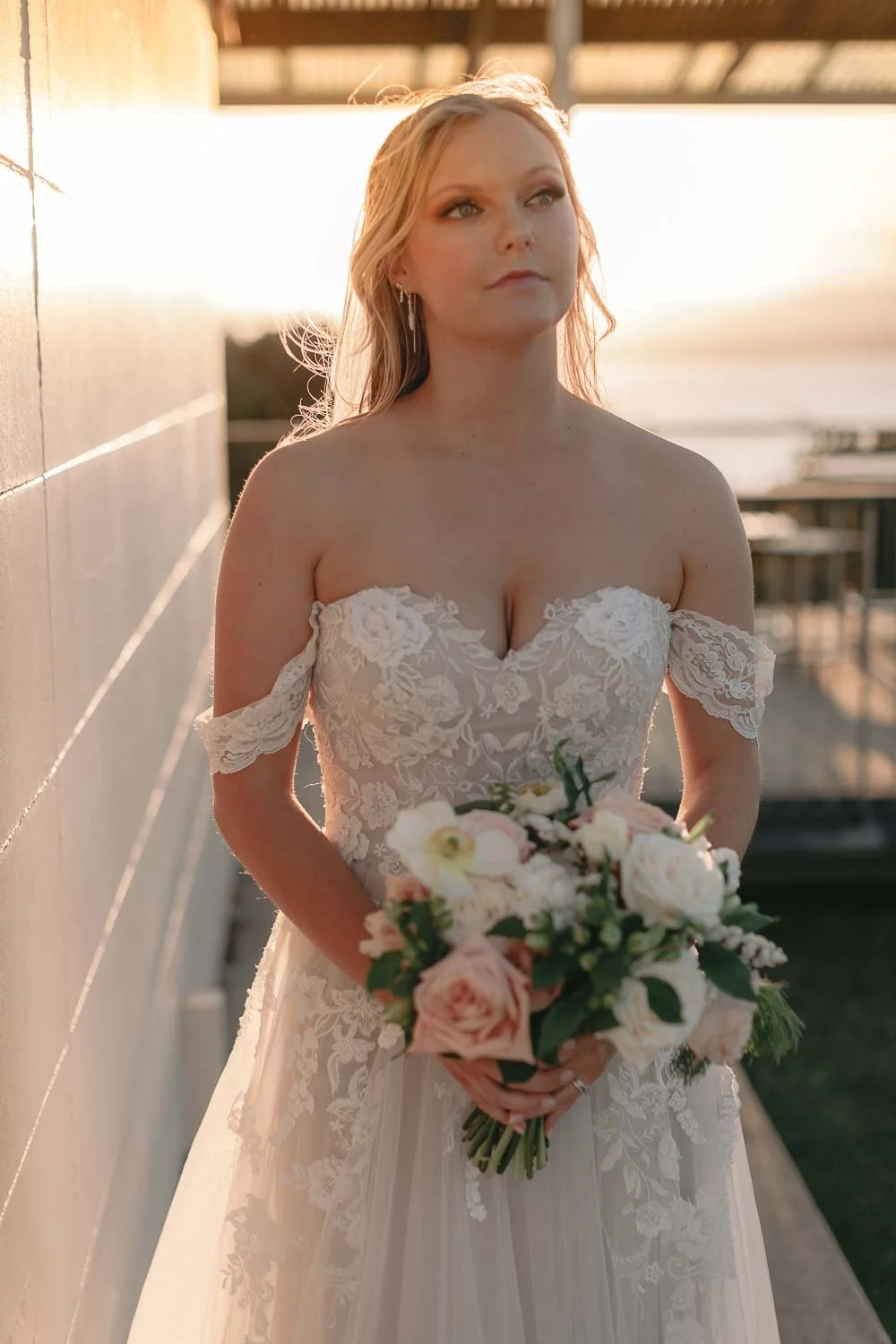 Bride in an off-the-shoulder gown holding her bouquet at the Cape Byron Lighthouse