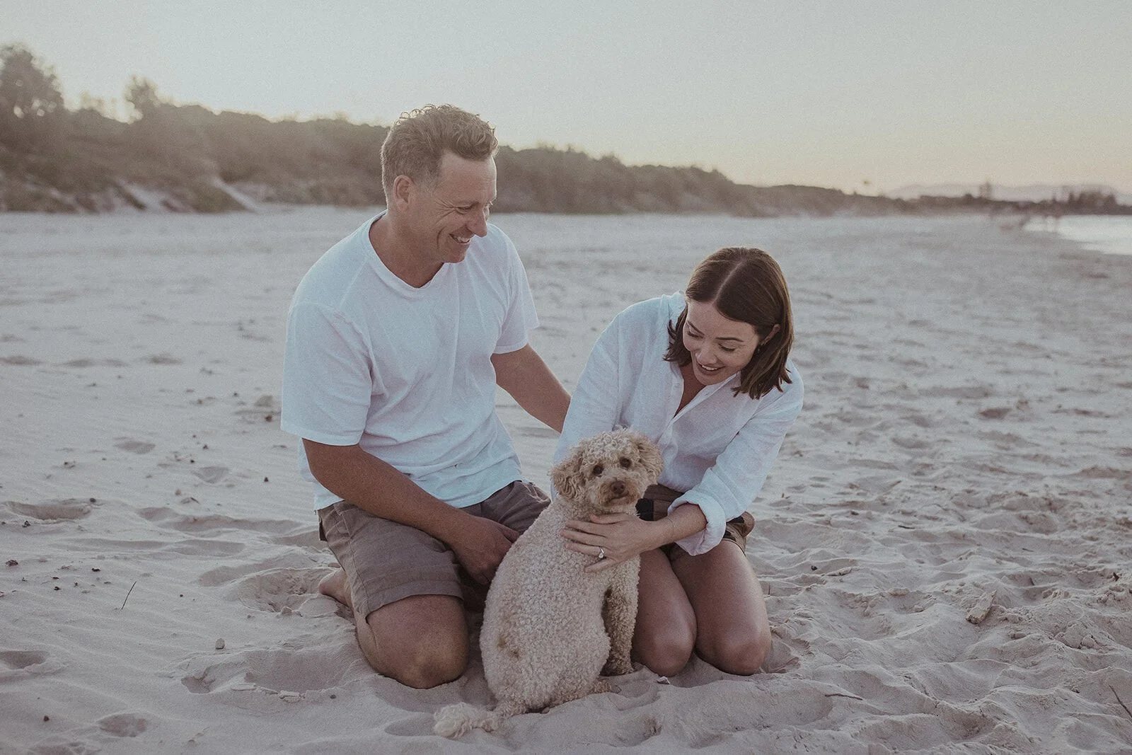 Couple patting their dog on the beach, Jamie and Jessica's beach marriage proposal at Belongil Beach, Byron Bay