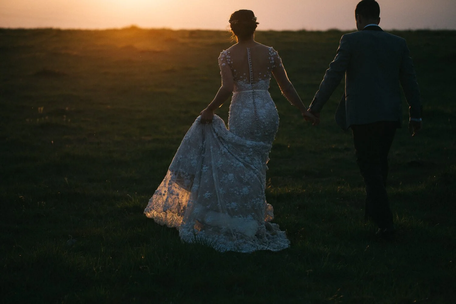 Bride and groom walking into the sunset across the paddocks at Bendooley Estate