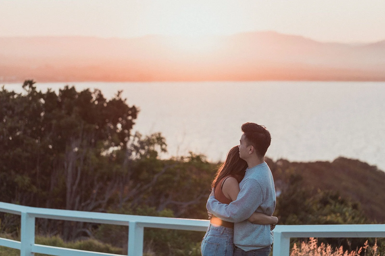 Couple embracing at the lookout fence with the bay behind, Douglas and Ying's sunset marriage proposal at Cape Byron Lighthouse, Byron Bay