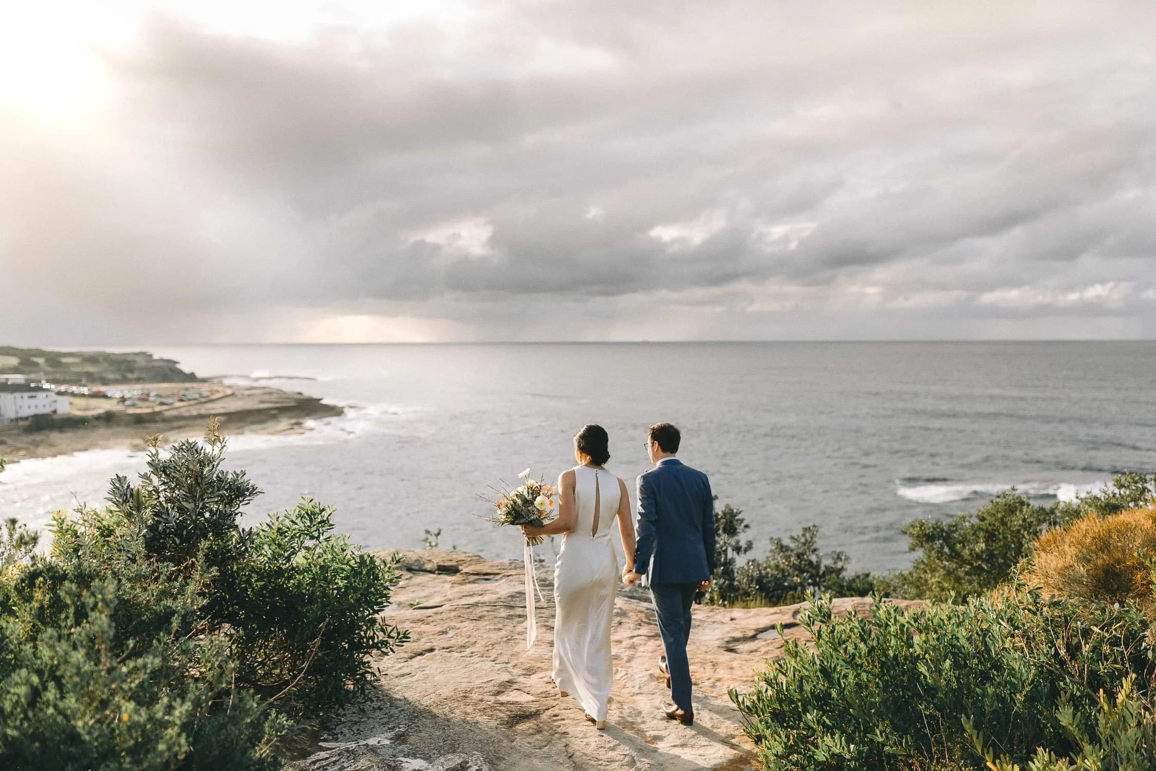 Bride and groom walking the clifftop path above the sea at Coogee, Sydney