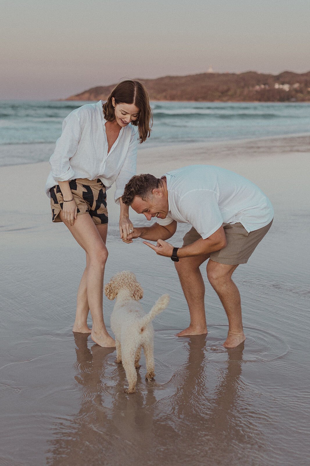 Couple looking at the ring in the shallows as their dog stands by, Jamie and Jessica's beach marriage proposal at Belongil Beach, Byron Bay