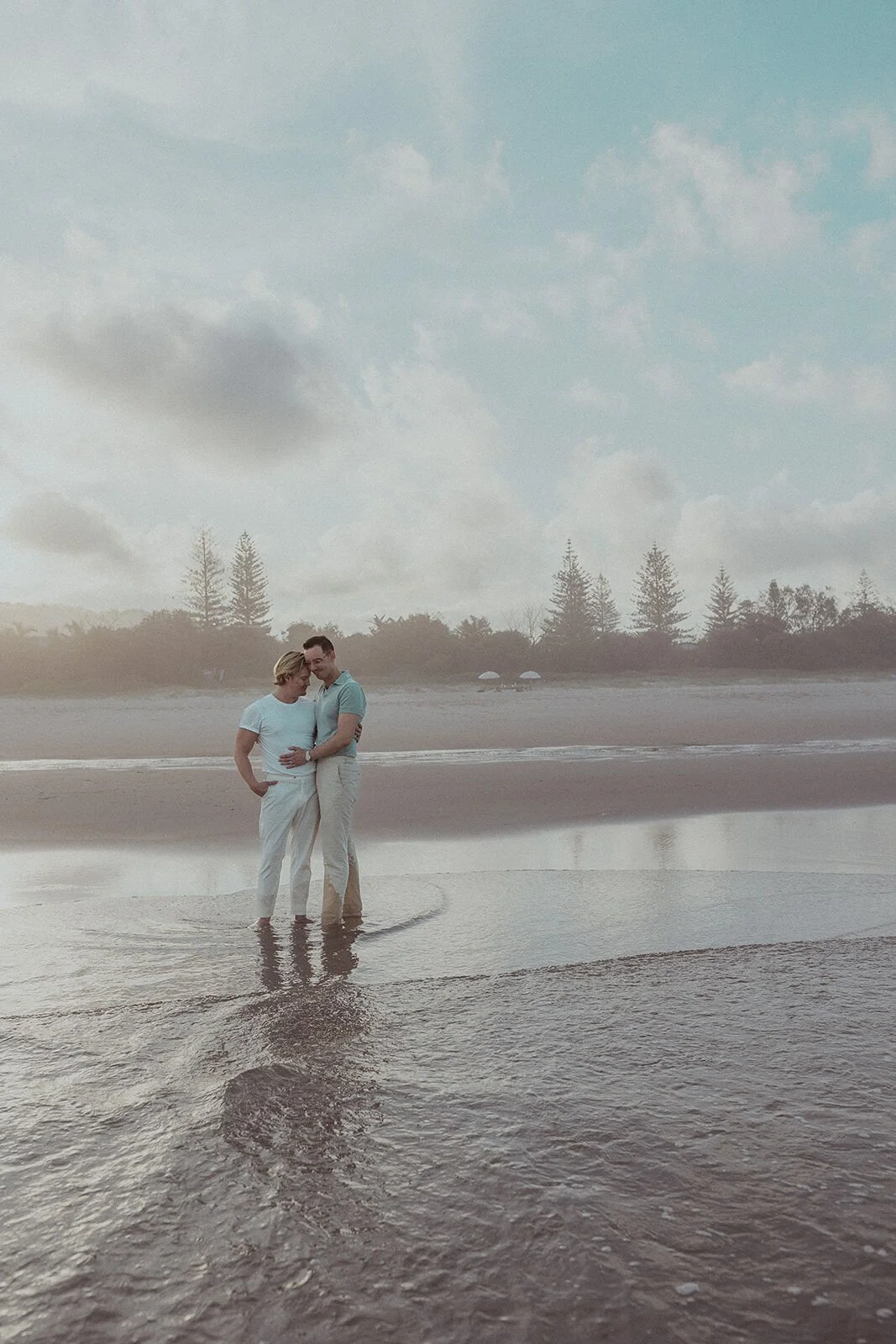 Couple embracing in the distance at the water's edge, Byron and Luke's marriage proposal at Cabarita Beach, Northern Rivers