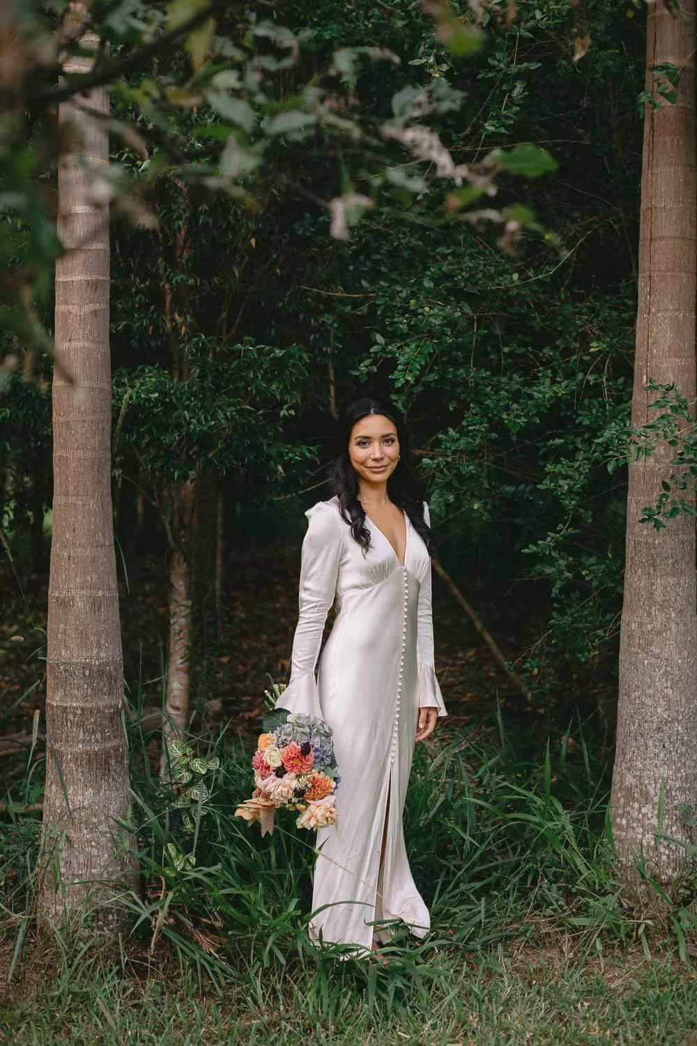 Bride standing among palm trunks in a subtropical garden in the Byron hinterland