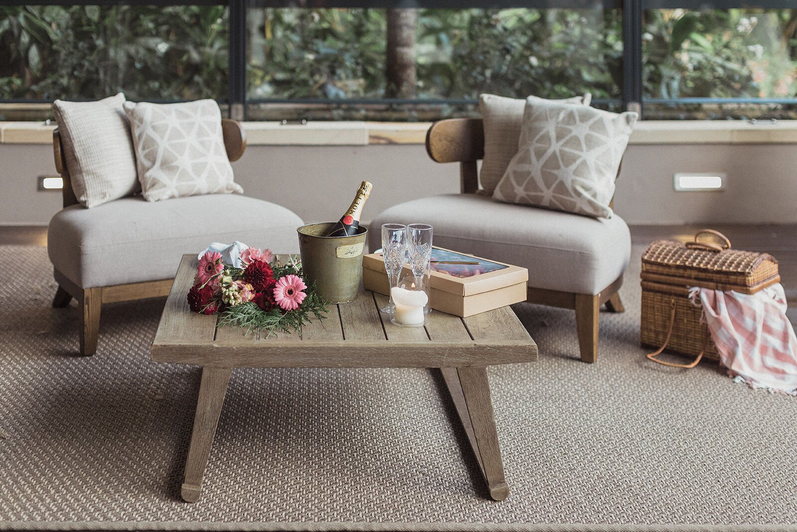 Timber coffee table with champagne in a bucket and bright flowers on the deck, Ben and Chloe's marriage proposal in Byron Bay