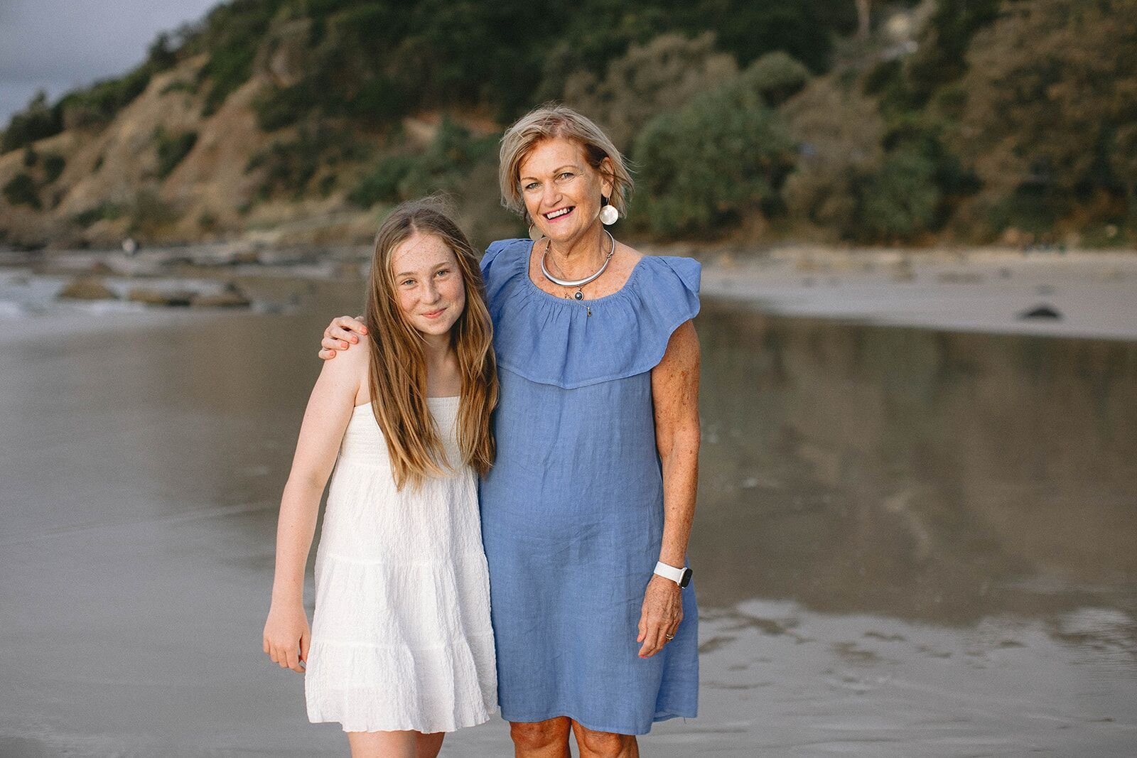 Grandmother in a blue dress with her arm around her teenage granddaughter, Wategos Beach