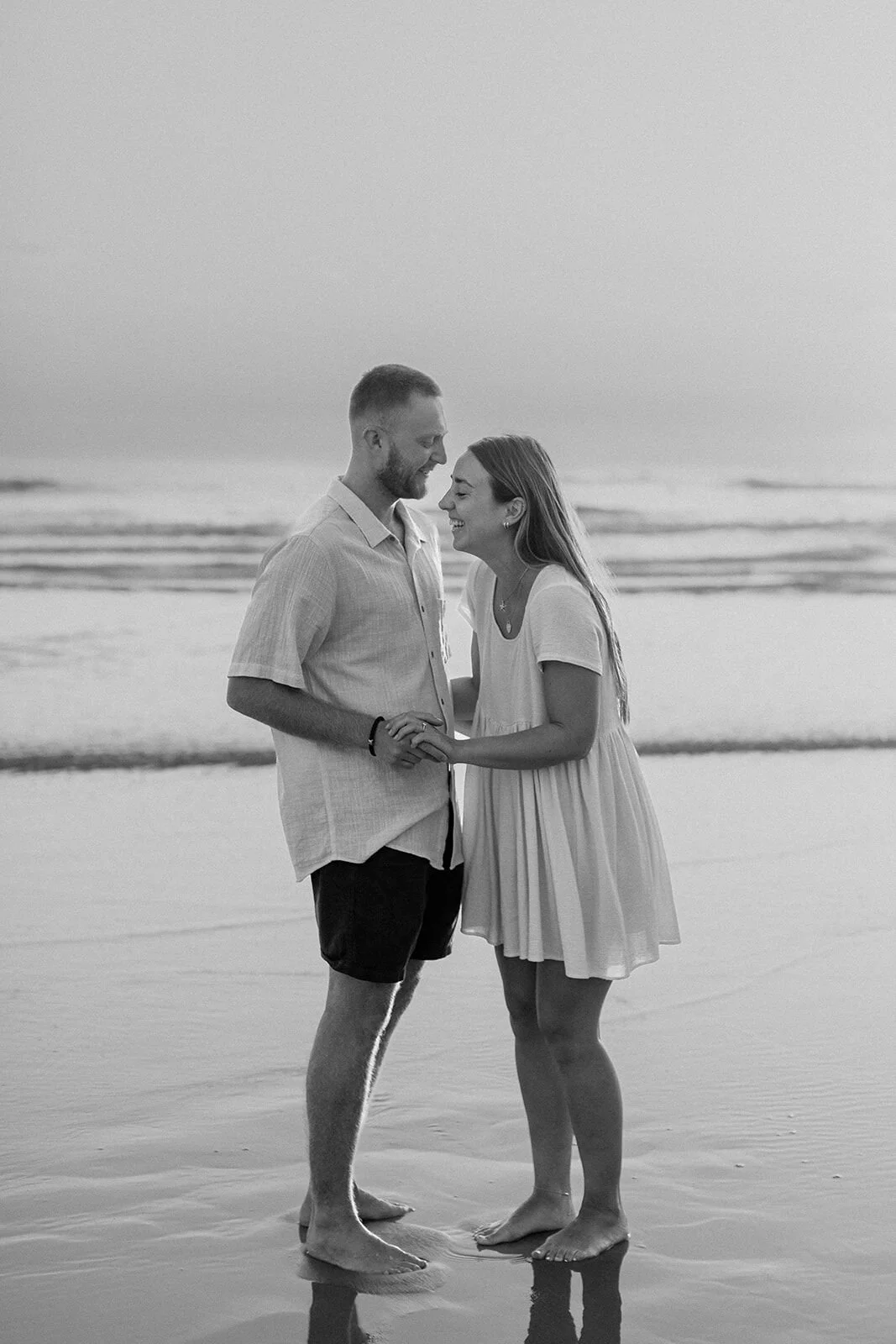 Black and white of the couple nose to nose, barefoot at the water's edge, Charlie and Hannah's sunrise marriage proposal at Broken Head Beach, Byron Bay