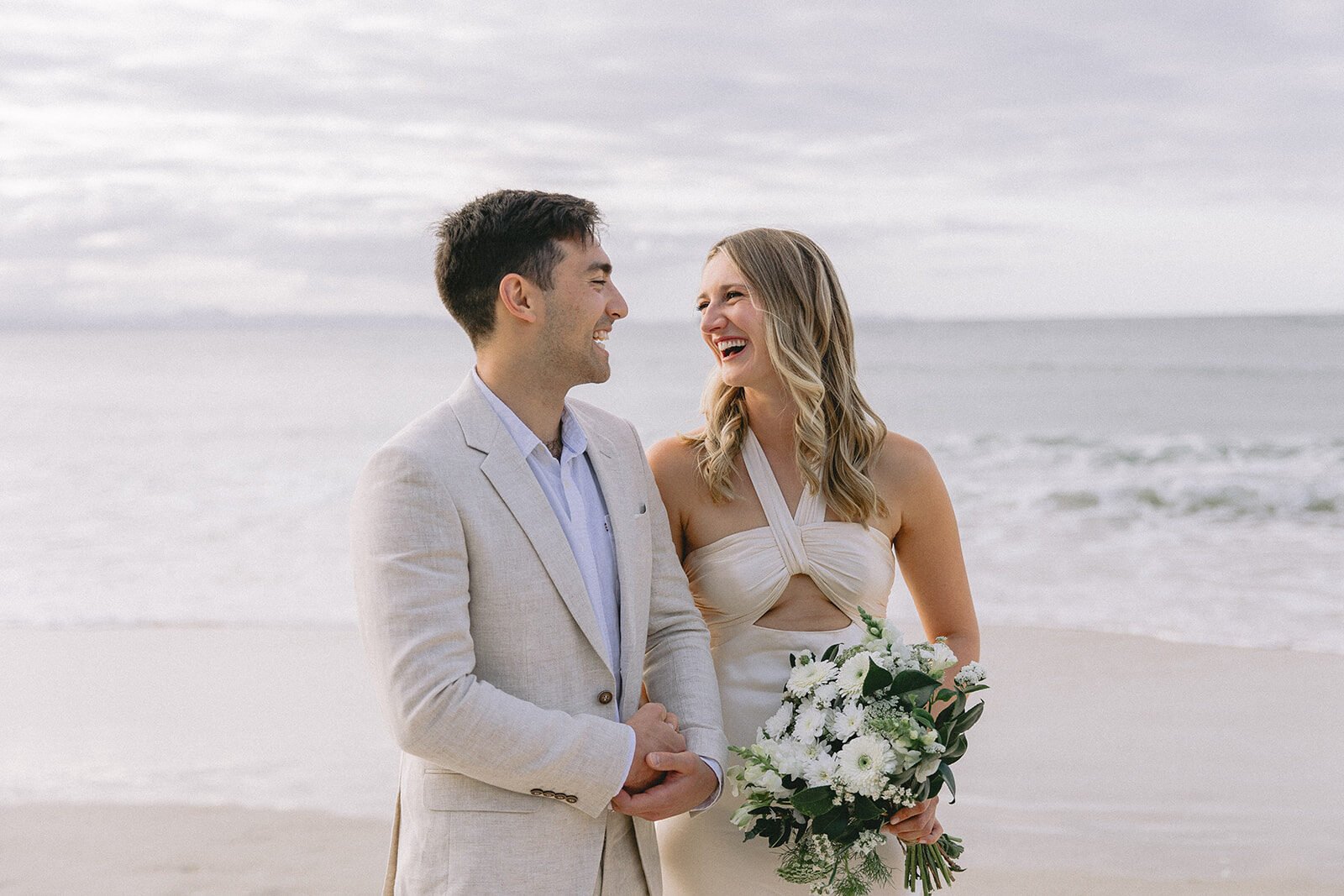 Bride laughing with the groom as she holds her bouquet, Abby and James' elopement at Little Wategos Beach, Byron Bay