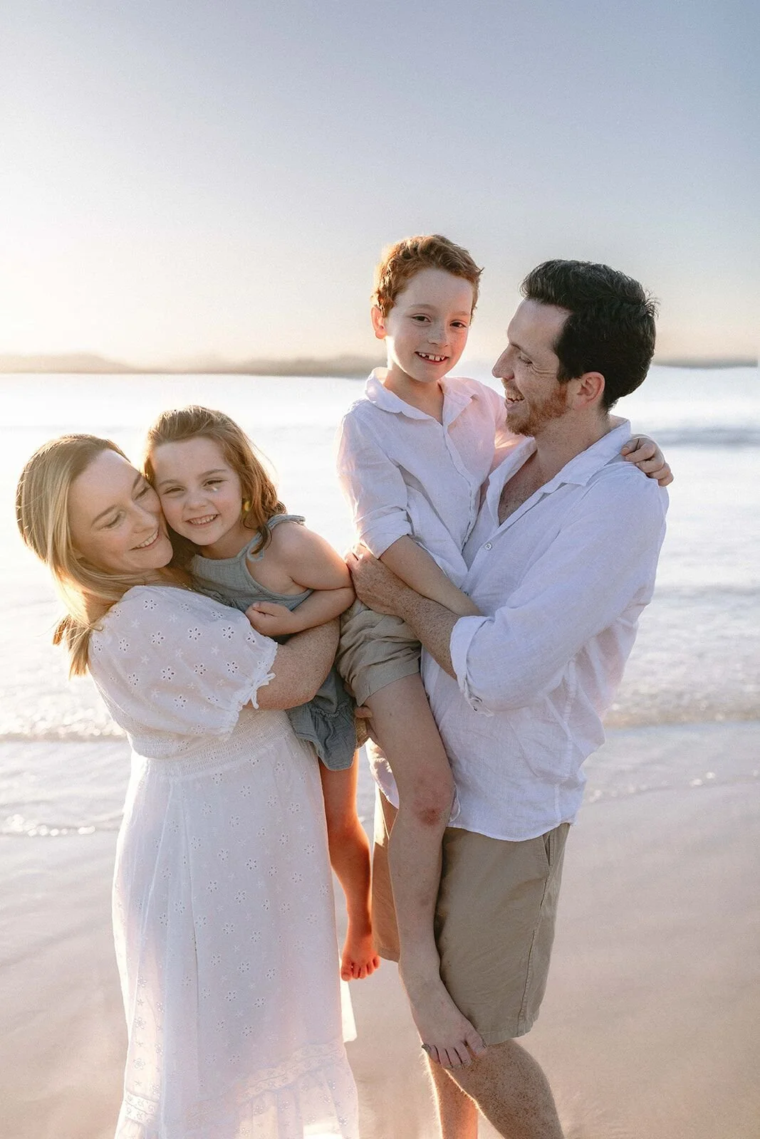 Parents cuddling their son and daughter close in golden evening light on the beach