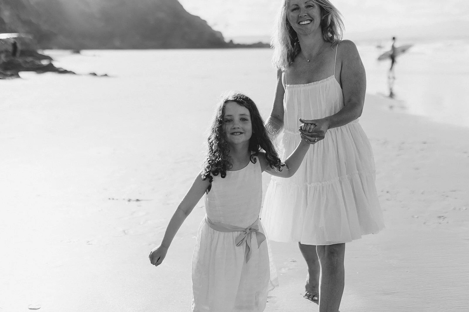 Black and white photo of a girl running along the sand holding her mum's hand, Wategos Beach