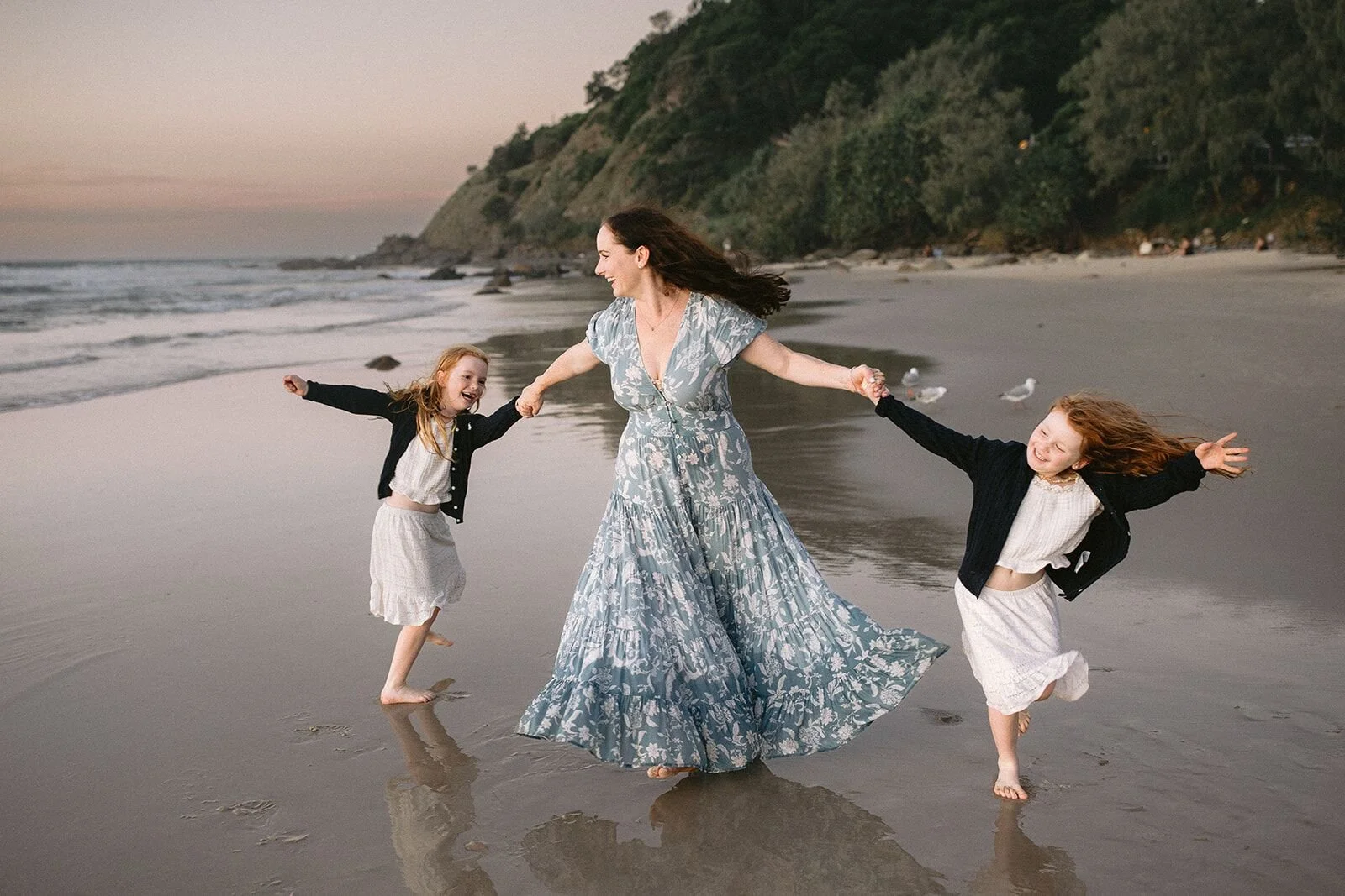 Mum spinning with her two daughters, holding hands, on the wet sand at Wategos Beach