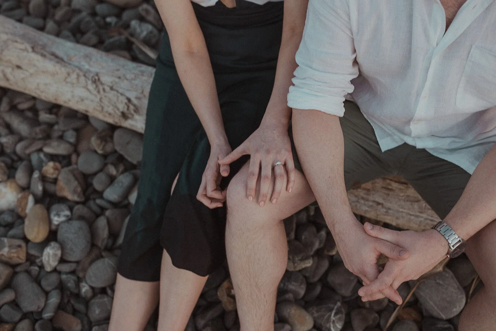 Close up of the couple's hands and engagement ring on a driftwood log among the pebbles, John and Emma's sunset marriage proposal at Wategos Beach, Byron Bay