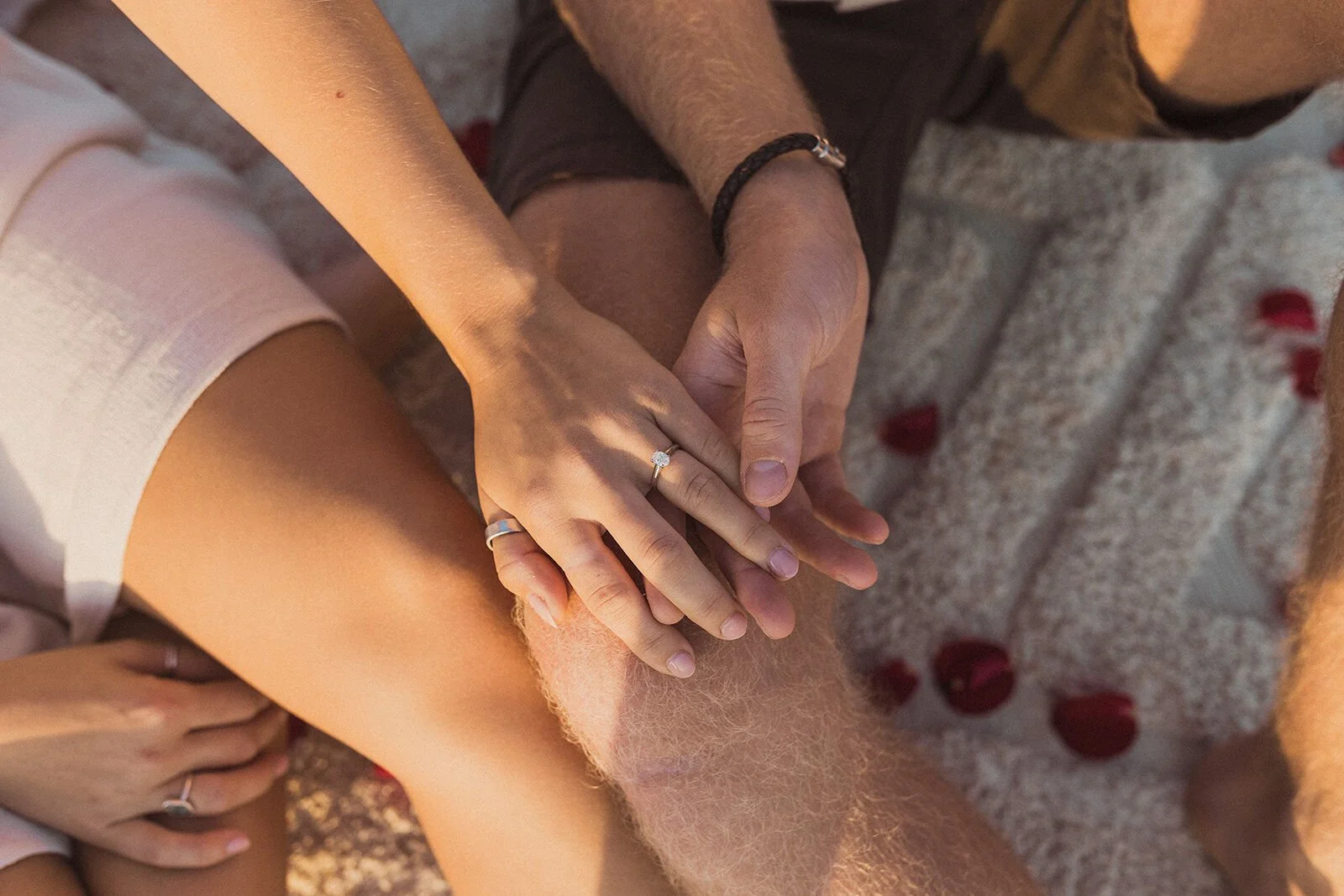 Close up of their hands and engagement ring over scattered rose petals, Charlie and Hannah's sunrise marriage proposal at Broken Head Beach, Byron Bay