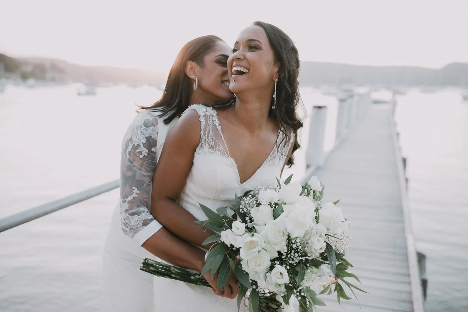 Two brides laughing together on the jetty at Beach House Avalon