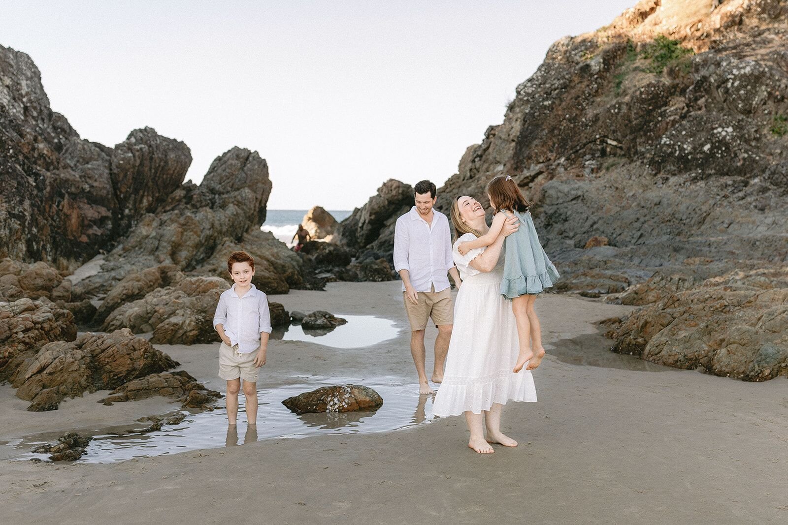Family walking among the rocks and a tidal pool at The Pass, Byron Bay
