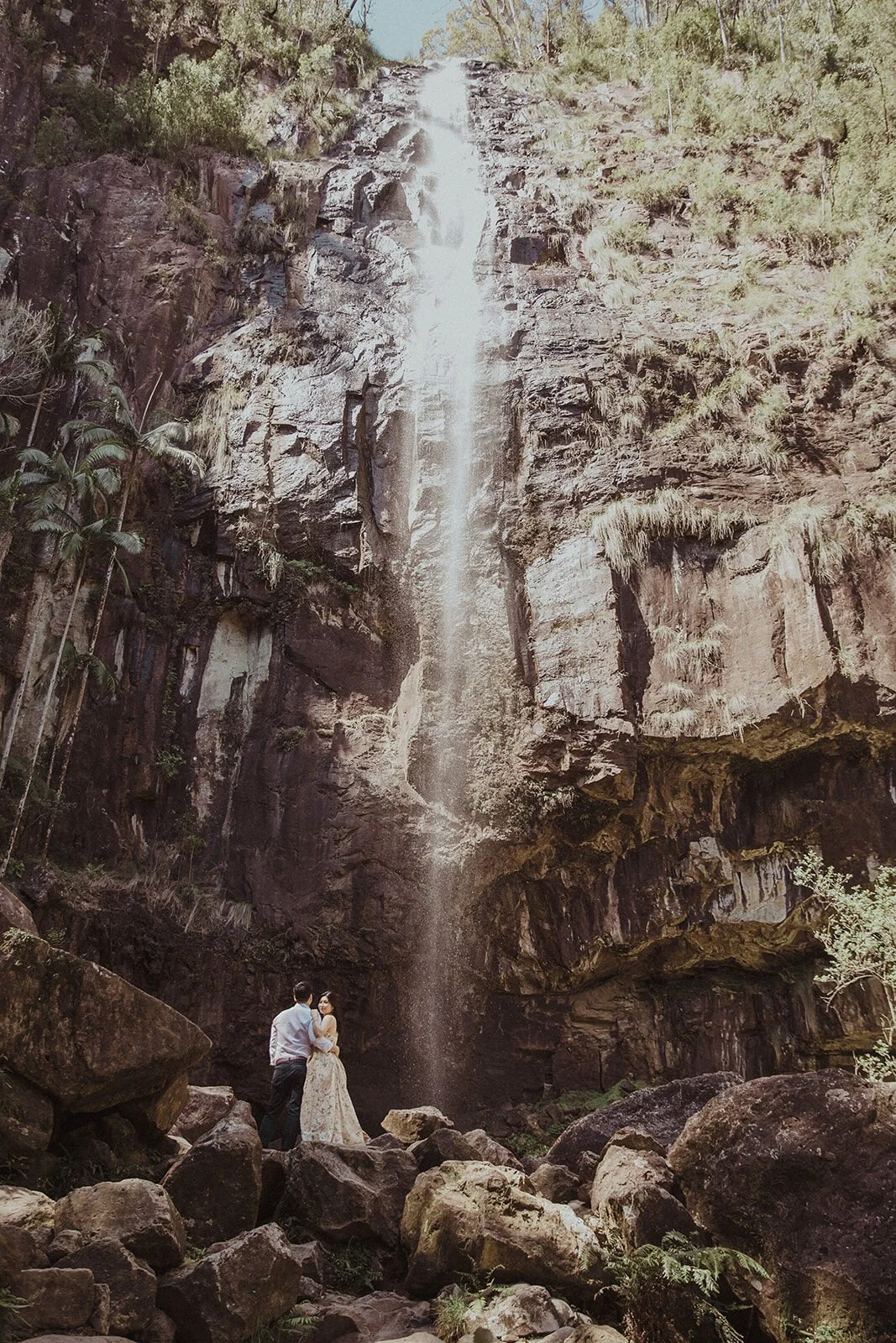 Couple kissing beneath a tall waterfall, Maggie and William's pre-wedding photos in Byron Bay